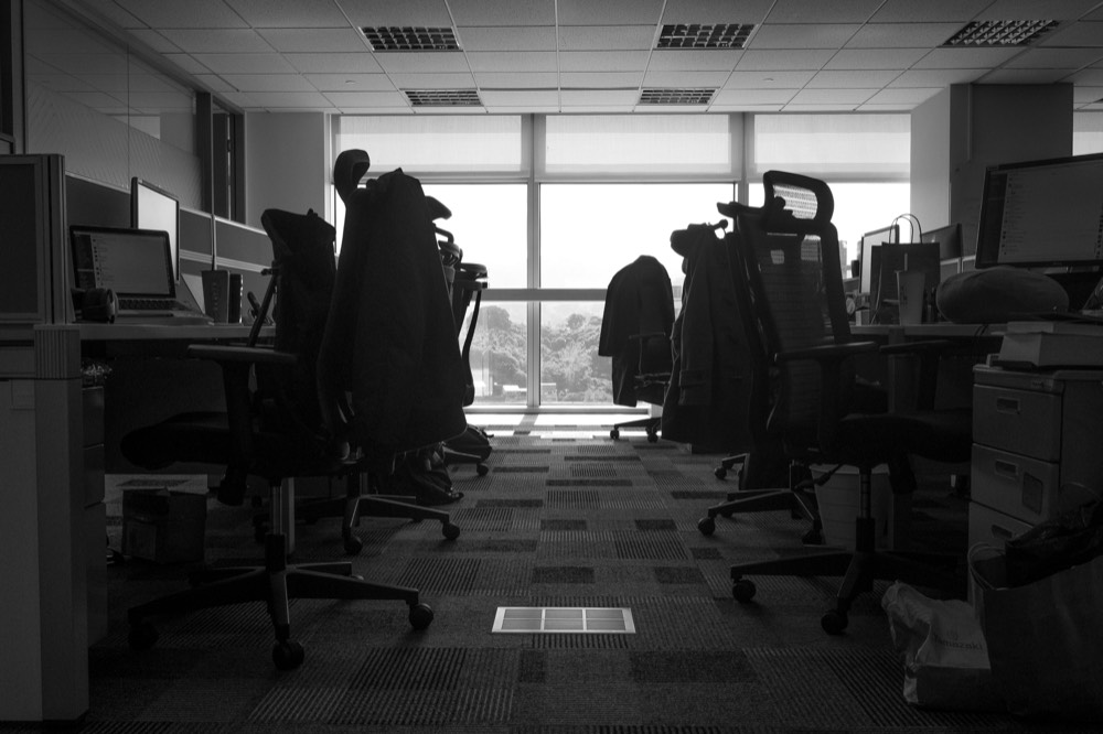 An empty office at dusk, chairs pushed back and the lights off